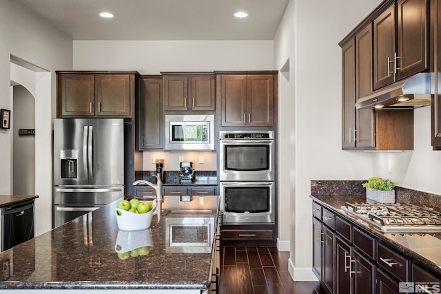 kitchen featuring appliances with stainless steel finishes, arched walkways, under cabinet range hood, and dark stone countertops