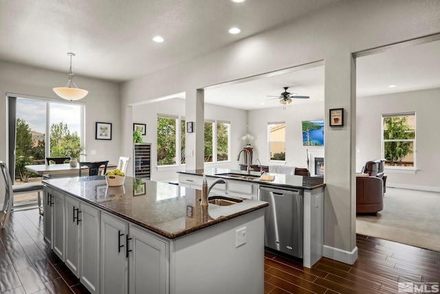 kitchen with stainless steel dishwasher, wood finish floors, a sink, and a center island with sink