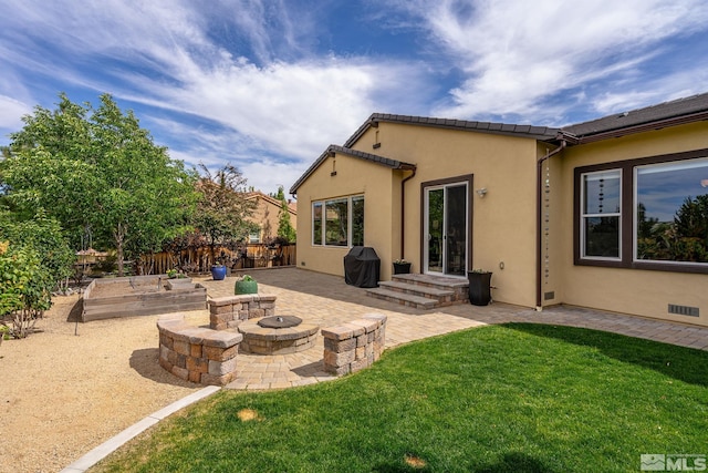 rear view of house featuring a patio, a fire pit, fence, a lawn, and stucco siding