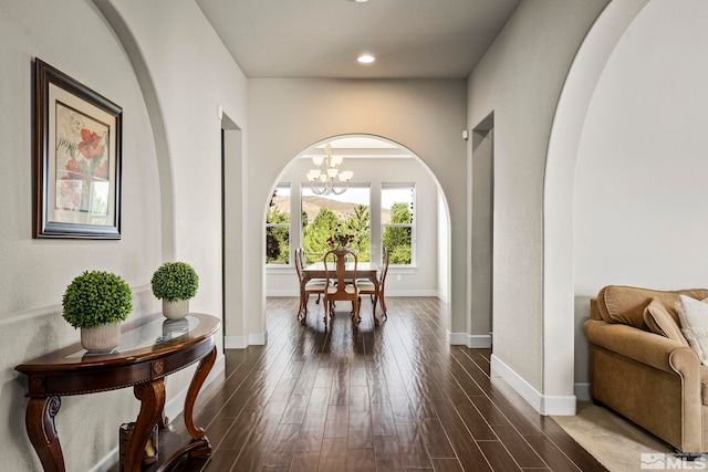 interior space featuring dark wood-style floors, a notable chandelier, arched walkways, and baseboards