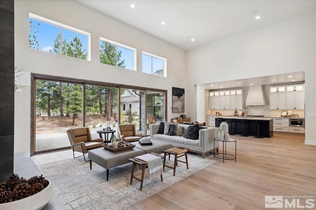 living room with plenty of natural light, light hardwood / wood-style floors, a high ceiling, and sink