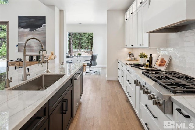 kitchen featuring white cabinets, sink, light hardwood / wood-style flooring, light stone countertops, and custom range hood