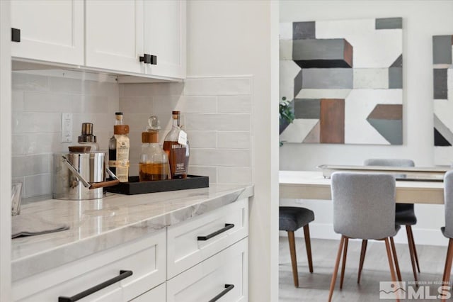 bar with light stone counters, white cabinetry, and backsplash