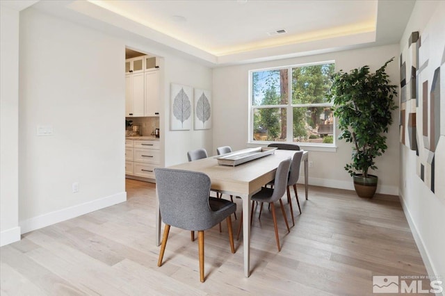 dining space featuring light hardwood / wood-style floors and a tray ceiling