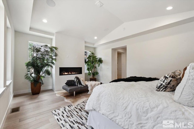 bedroom featuring a fireplace, light hardwood / wood-style flooring, and lofted ceiling