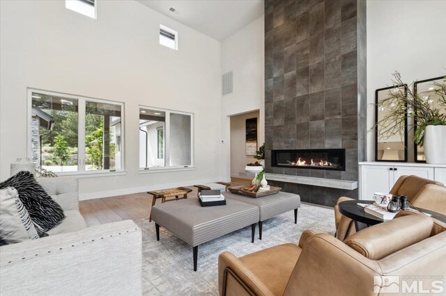 living room featuring a towering ceiling, a tile fireplace, and light hardwood / wood-style flooring