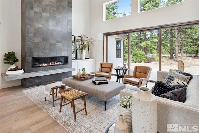 living room with a high ceiling, a tile fireplace, and light hardwood / wood-style flooring