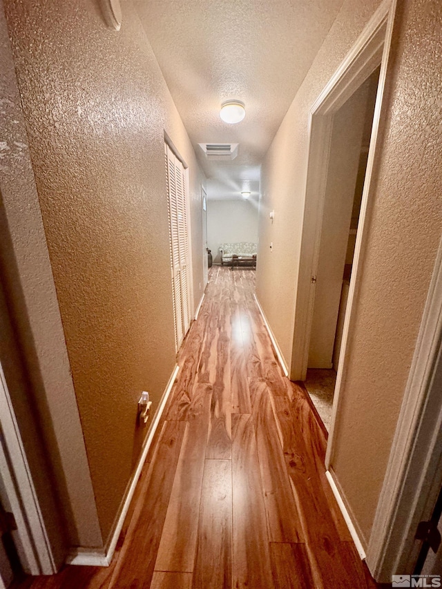 hall with wood-type flooring and a textured ceiling