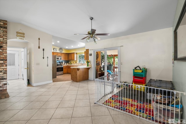 interior space with light tile patterned floors, ceiling fan, stove, vaulted ceiling, and kitchen peninsula