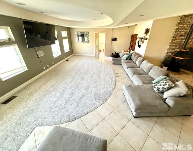 living room with brick wall, a wood stove, light tile patterned floors, and a tray ceiling