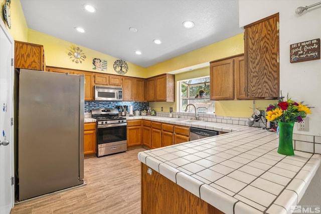 kitchen featuring tasteful backsplash, tile counters, light hardwood / wood-style floors, appliances with stainless steel finishes, and lofted ceiling