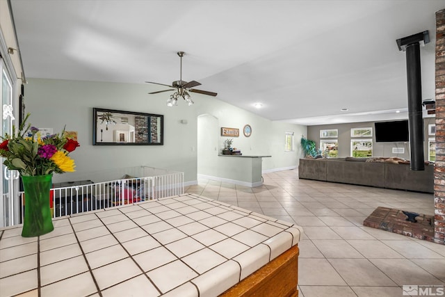 unfurnished living room with a wood stove, light tile patterned floors, lofted ceiling, and ceiling fan