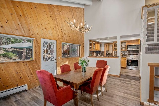 dining area featuring a baseboard radiator, light hardwood / wood-style flooring, wood walls, a towering ceiling, and a chandelier