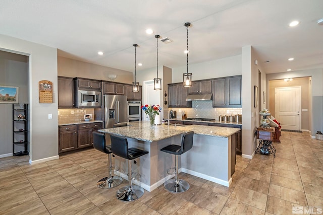 kitchen with dark brown cabinetry, a breakfast bar, light stone counters, a center island with sink, and appliances with stainless steel finishes