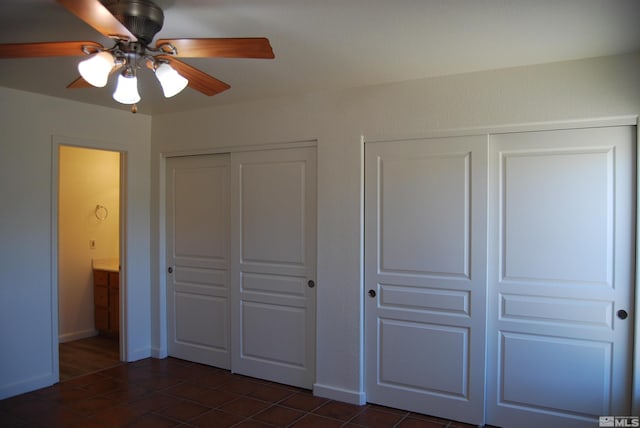 unfurnished bedroom featuring dark tile patterned flooring, ceiling fan, and multiple closets