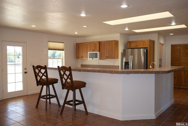 kitchen featuring a textured ceiling, stainless steel fridge with ice dispenser, a kitchen island, tile counters, and a breakfast bar area