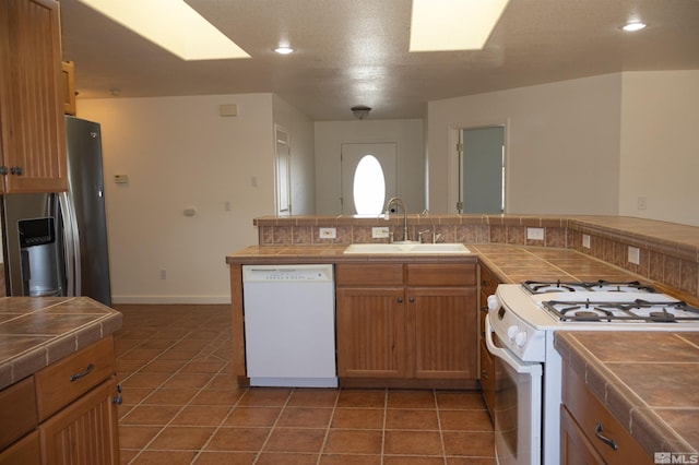 kitchen featuring tile countertops, dark tile patterned floors, white appliances, and sink