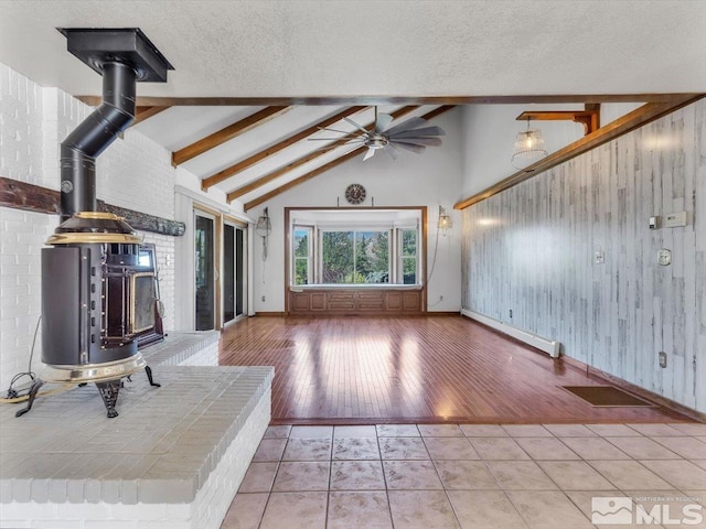 unfurnished living room with a wood stove, wooden walls, lofted ceiling with beams, and a baseboard radiator