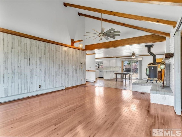 unfurnished living room with baseboard heating, a wood stove, light hardwood / wood-style flooring, and beamed ceiling