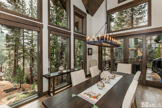 dining room with high vaulted ceiling, light wood-type flooring, and a notable chandelier