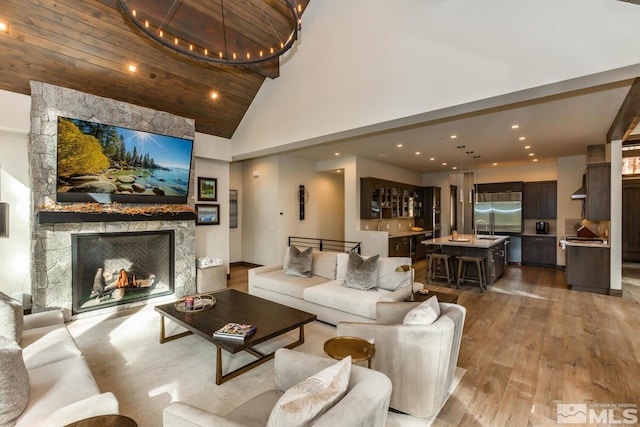 living room with wood ceiling, a stone fireplace, high vaulted ceiling, and light wood-type flooring