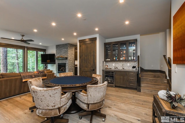 dining space featuring a stone fireplace, bar area, light wood-type flooring, ceiling fan, and beverage cooler