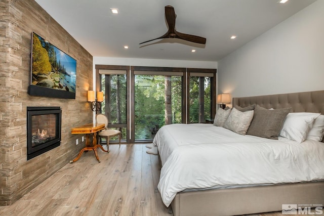 bedroom with light wood-type flooring, a fireplace, and ceiling fan