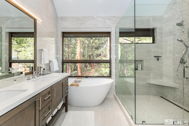 bathroom with independent shower and bath, vanity, a wealth of natural light, and tile walls