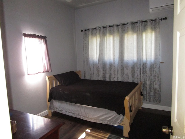 bedroom featuring a wall unit AC, wood finished floors, and baseboards