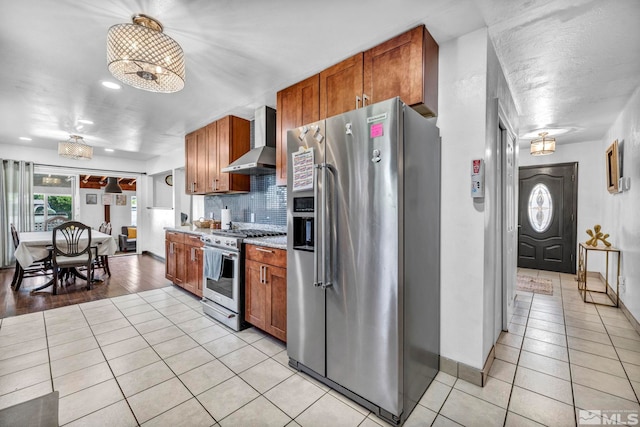 kitchen with light tile patterned floors, backsplash, stainless steel appliances, a textured ceiling, and wall chimney exhaust hood