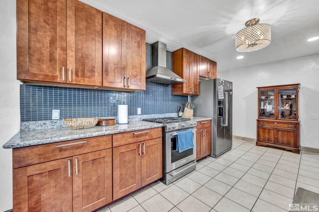 kitchen with wall chimney exhaust hood, light stone counters, light tile patterned floors, appliances with stainless steel finishes, and decorative backsplash