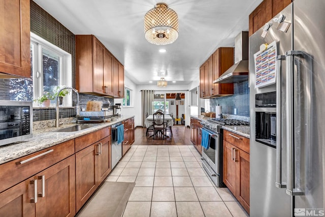 kitchen featuring wall chimney exhaust hood, sink, high end appliances, light stone counters, and a chandelier