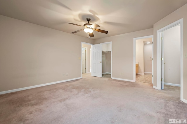 unfurnished bedroom with ceiling fan, light colored carpet, ensuite bath, a walk in closet, and a closet