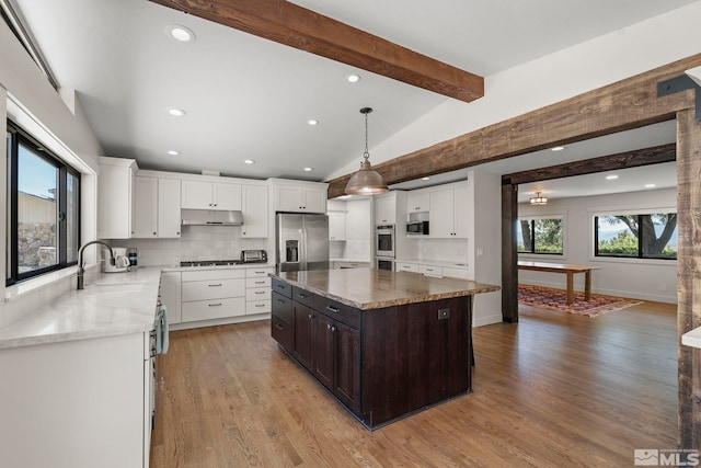 kitchen with lofted ceiling with beams, tasteful backsplash, decorative light fixtures, a kitchen island, and stainless steel appliances