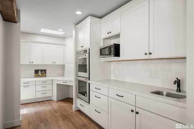 kitchen featuring a skylight, double oven, sink, hardwood / wood-style flooring, and white cabinets