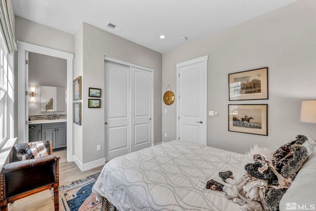 bedroom with ensuite bath, light wood-type flooring, sink, and a closet