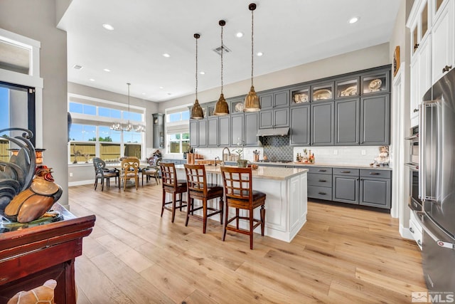 kitchen with a kitchen breakfast bar, tasteful backsplash, a kitchen island with sink, pendant lighting, and gray cabinets