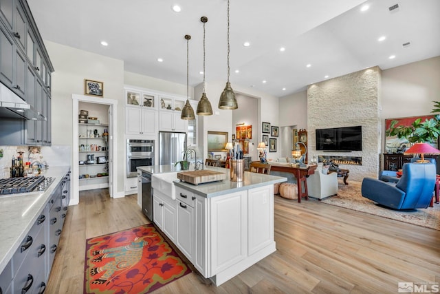 kitchen with gray cabinetry, white cabinetry, hanging light fixtures, light hardwood / wood-style flooring, and a center island with sink