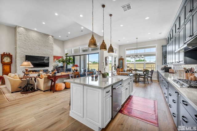 kitchen with sink, light hardwood / wood-style floors, pendant lighting, a kitchen island with sink, and appliances with stainless steel finishes