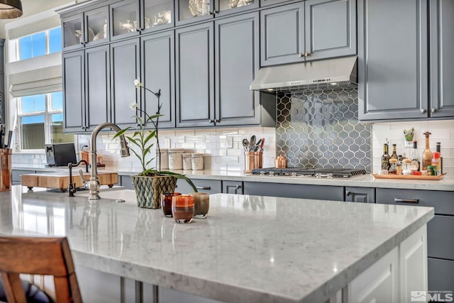 kitchen with tasteful backsplash, gray cabinets, light stone countertops, and stainless steel gas stovetop