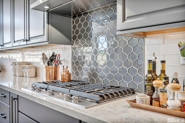 kitchen with backsplash, gray cabinets, range hood, and stainless steel gas cooktop