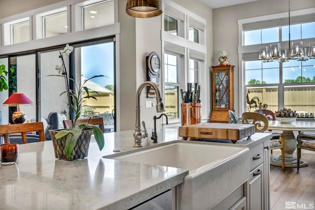 kitchen featuring an inviting chandelier, sink, hanging light fixtures, light stone countertops, and light wood-type flooring