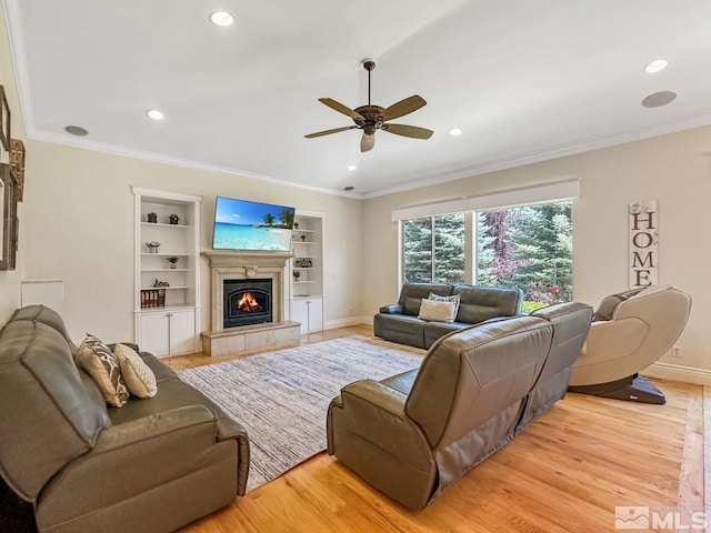 living room with light wood-type flooring, a tiled fireplace, crown molding, and built in features