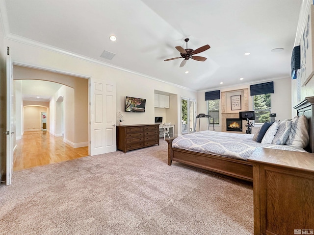 carpeted bedroom featuring ceiling fan, a large fireplace, and crown molding