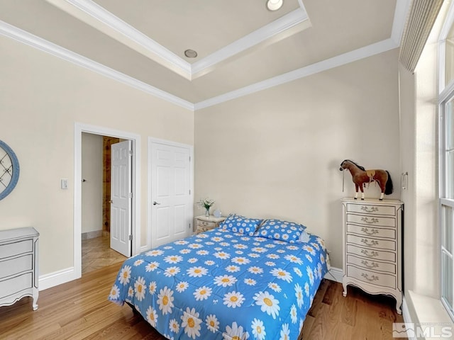 bedroom featuring wood-type flooring, ornamental molding, and a raised ceiling