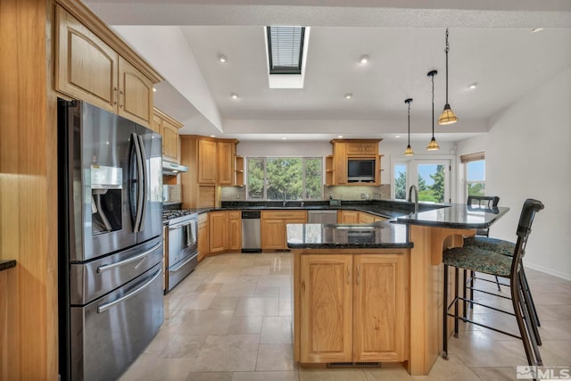 kitchen featuring appliances with stainless steel finishes, a center island, decorative light fixtures, and dark stone countertops