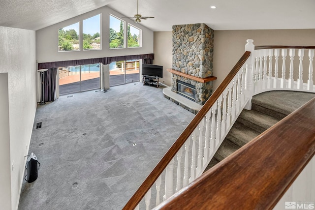 carpeted living room featuring ceiling fan, a stone fireplace, lofted ceiling, and a textured ceiling