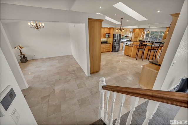 interior space with a skylight, a chandelier, decorative light fixtures, a breakfast bar area, and appliances with stainless steel finishes