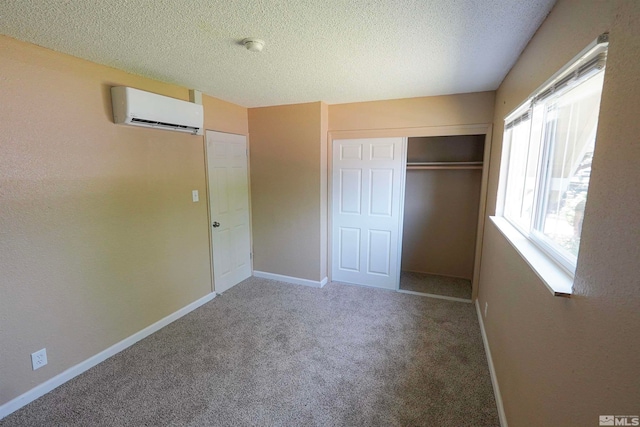 unfurnished bedroom with carpet floors, a textured ceiling, a wall unit AC, and a closet