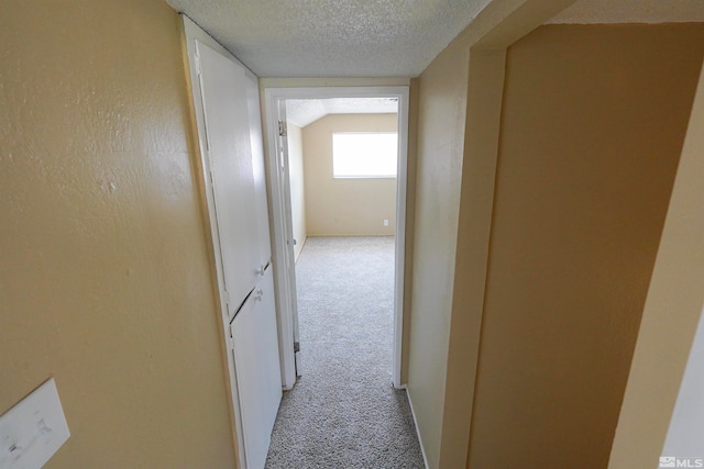 hall featuring light colored carpet, lofted ceiling, and a textured ceiling